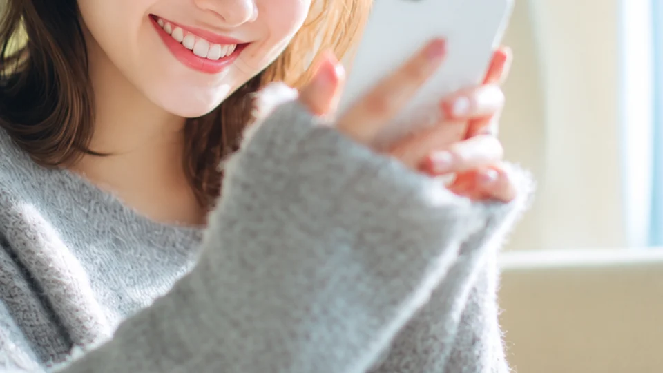 スマホを持って笑顔で話す口元と手元（イメージ）